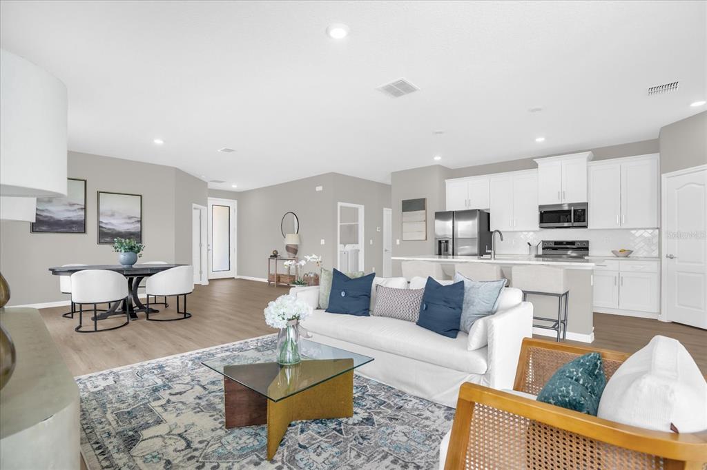 An open-concept living room and kitchen featuring white cabinetry, light wood flooring, and neutral decor — 5834 ESCALON DRIVE, SEBRING, FL