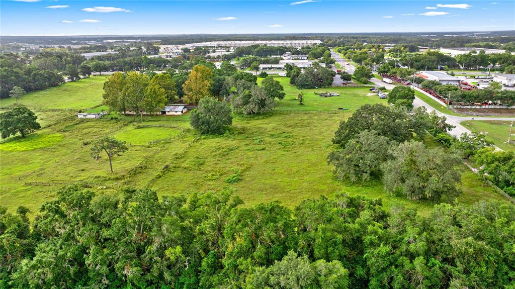 An aerial view shows a large, grassy field with scattered trees and a small house — NW 52ND AVENUE, OCALA, FL