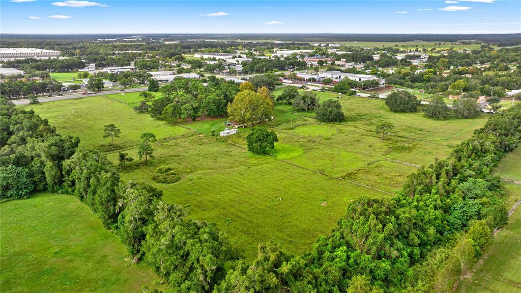 An aerial view shows a large, grassy lot surrounded by trees with a small house — NW 52ND AVENUE, OCALA, FL