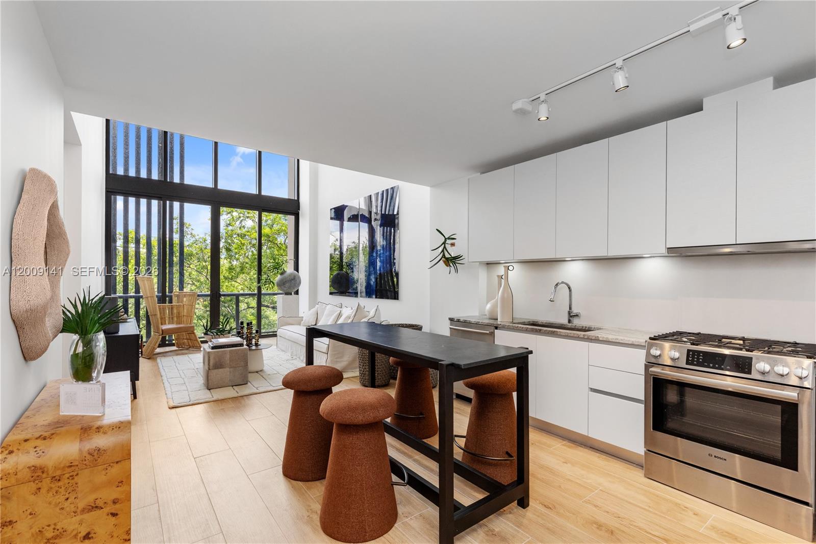 A modern kitchen and living area features white cabinetry, a black island, and floor-to-ceiling windows — 3034 Oak Avenue, Coconut Grove FL 33133, COCONUT GROVE, FL