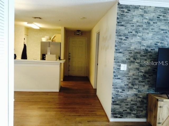 A view of a living area with wood-look flooring, a stone accent wall, and kitchen — 1919 SUMMER CLUB DRIVE UNIT 207, OVIEDO, FL