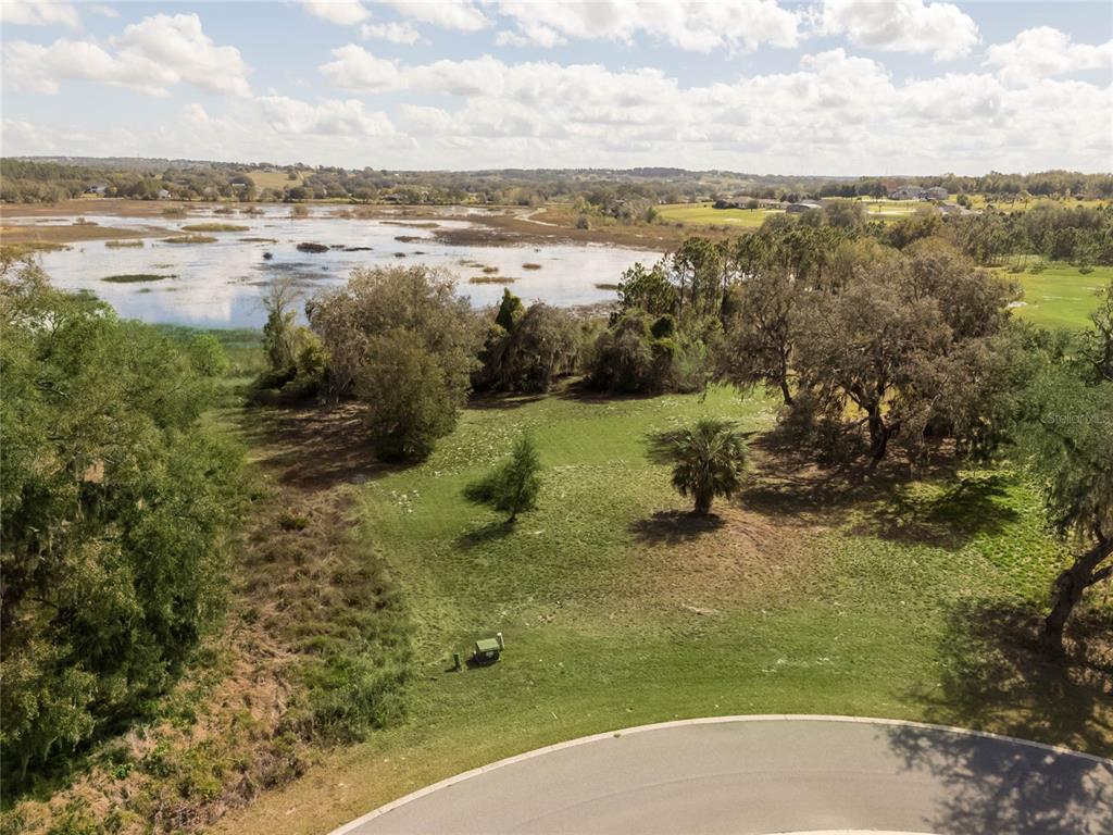 An aerial view shows a vacant, grassy lot bordering a large lake and wooded area — 476 LONG AND WINDING RD, HOWEY IN THE HILLS, FL