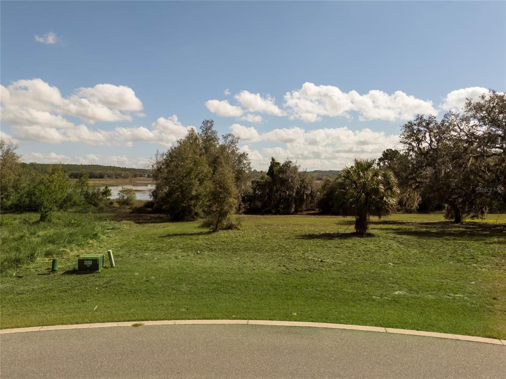 A grassy, undeveloped lot features scattered trees and a view of a distant pond — 476 LONG AND WINDING RD, HOWEY IN THE HILLS, FL