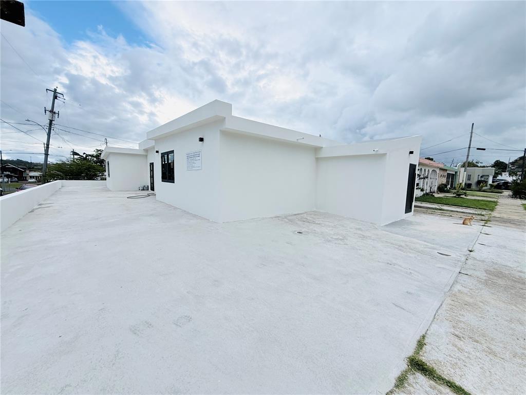A white, flat-roofed building exterior with a large concrete driveway under a cloudy sky — TRIPLEX HOUSE  Calle 5 D1 EXT. BUSO, HUMACAO, PR