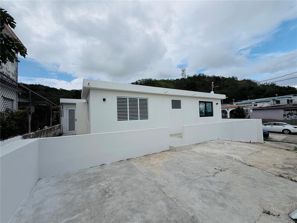 A white single-story house with a concrete driveway and a low perimeter wall — TRIPLEX HOUSE  Calle 5 D1 EXT. BUSO, HUMACAO, PR