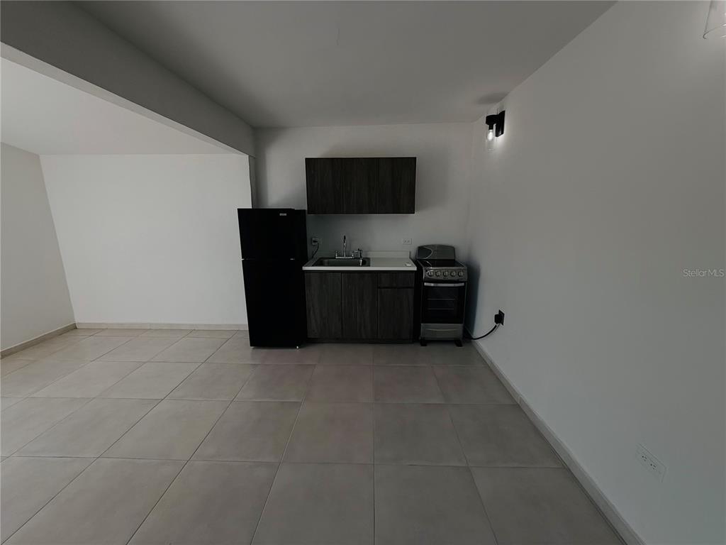 A small kitchen area features dark wood cabinets, a black refrigerator, and a compact stove — TRIPLEX HOUSE  Calle 5 D1 EXT. BUSO, HUMACAO, PR