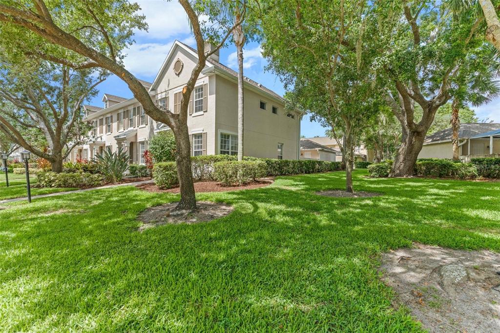 A multi-story tan townhouse exterior surrounded by green lawns and mature trees — 5650 DUVAL STREET, BRADENTON, FL