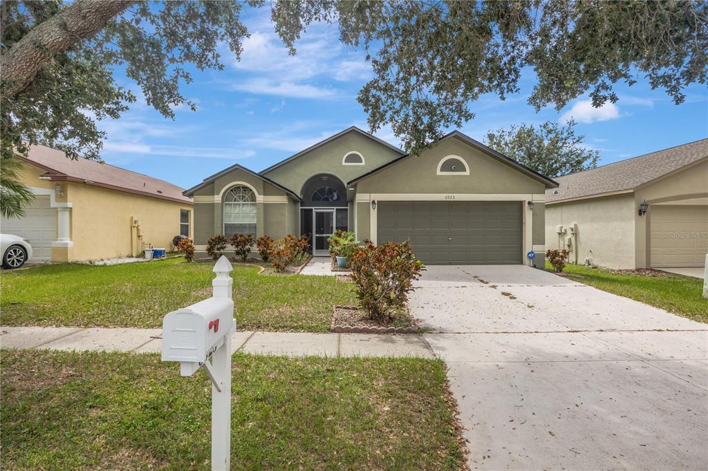 A single-story house with a green stucco exterior, a two-car garage, and a front lawn — 6923 WATERBROOK COURT, GIBSONTON, FL