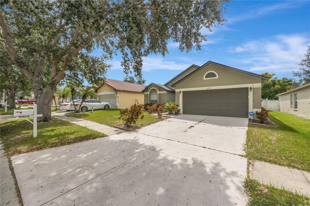 A single-story suburban house with a two-car garage, concrete driveway, and a large shade tree — 6923 WATERBROOK COURT, GIBSONTON, FL