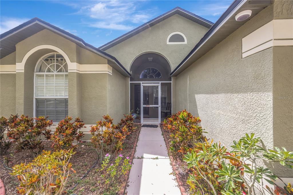 A walkway leads to the front entrance of a house with olive-colored stucco walls — 6923 WATERBROOK COURT, GIBSONTON, FL
