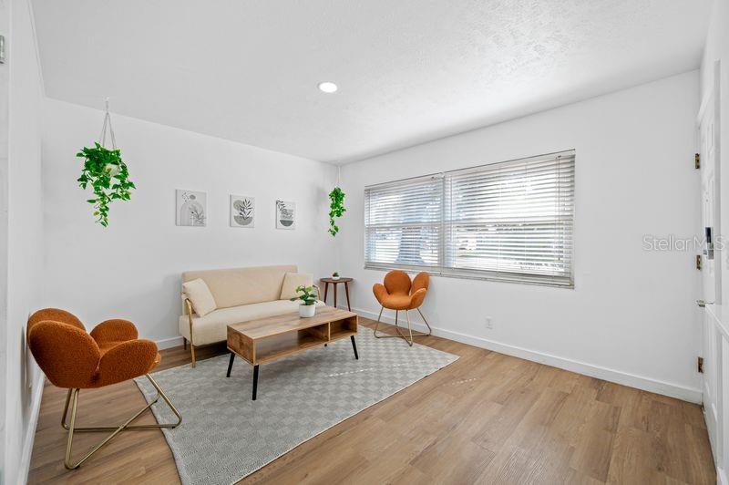 A living room features light wood flooring, a beige sofa, two orange chairs, and blinds — 4409 W PEARL AVENUE, TAMPA, FL