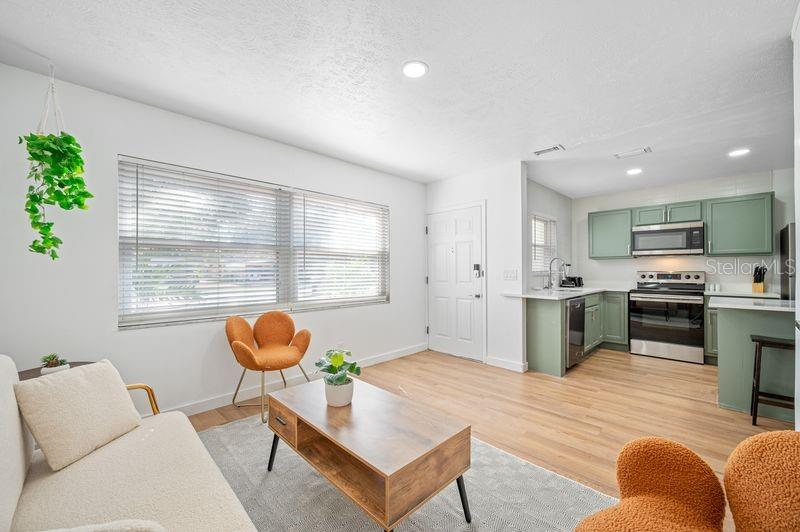 A living room with light wood floors flows into a kitchen with sage green cabinets — 4409 W PEARL AVENUE, TAMPA, FL