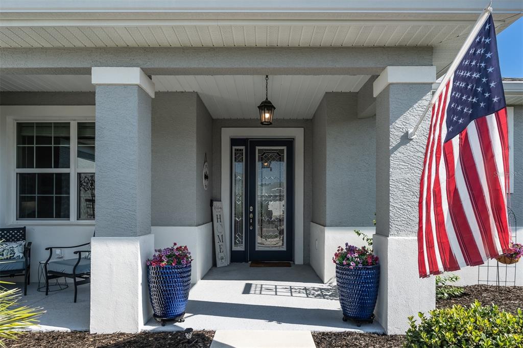 A covered front porch features a dark blue door, two blue planters, and an American flag — 10517 SW 90TH STREET ROAD, OCALA, FL