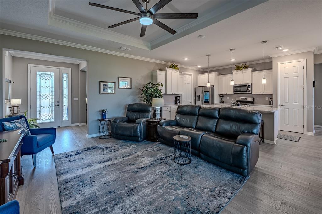 An open-concept living room features a leather sofa, recliner, area rug, and adjacent kitchen — 10517 SW 90TH STREET ROAD, OCALA, FL