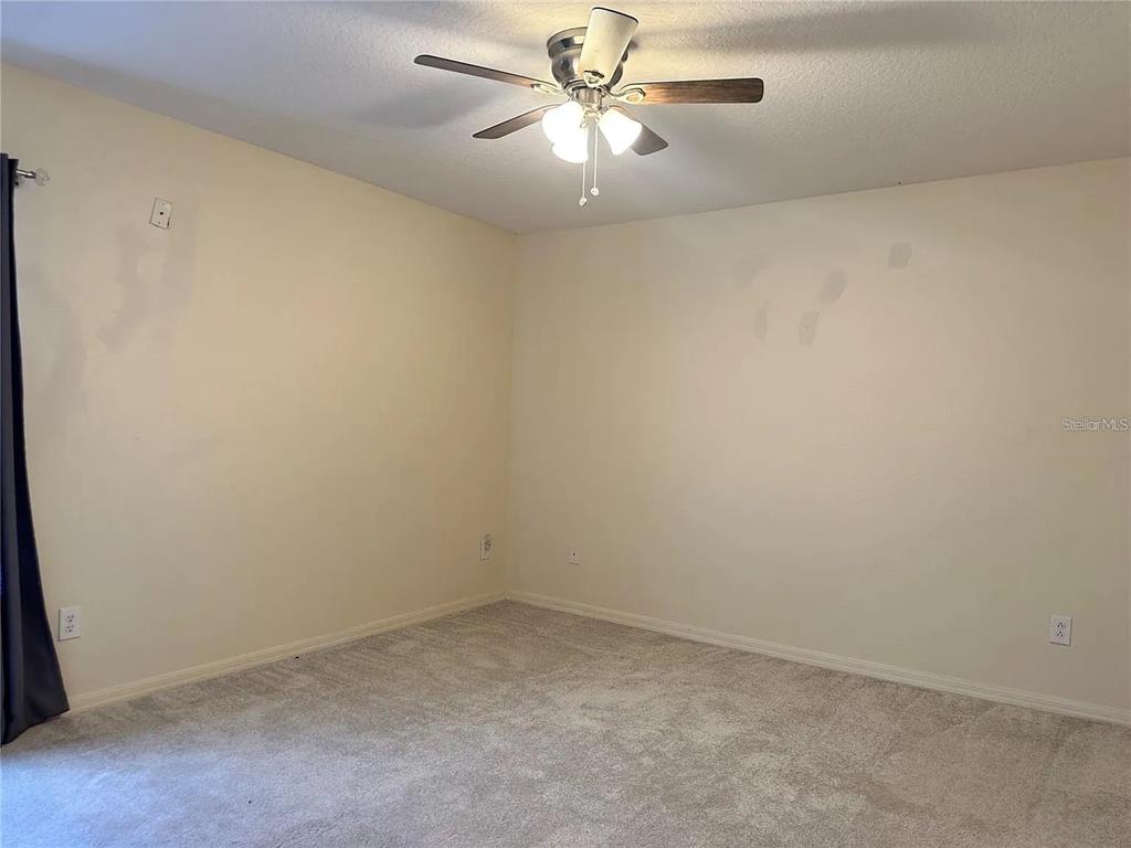 An empty bedroom features beige walls, light-colored carpeting, and a ceiling fan with lights — 7232 SEEDPOD LOOP, WESLEY CHAPEL, FL