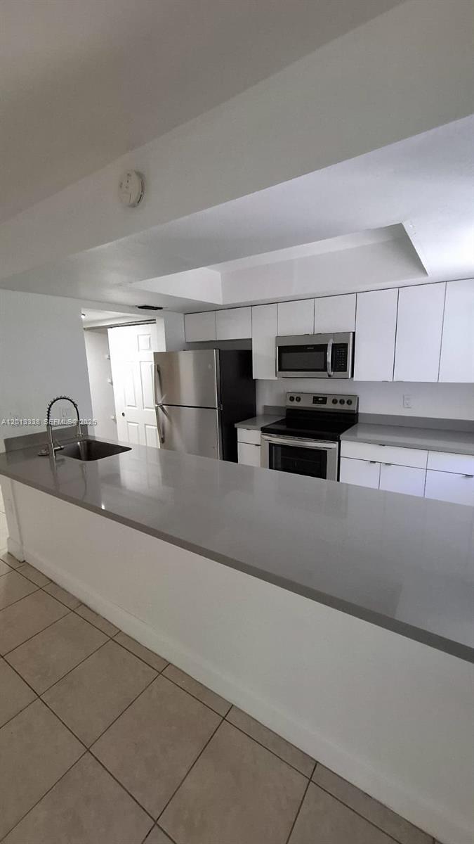 A kitchen features white cabinets, stainless steel appliances, and a gray countertop breakfast bar — 16220 NW 2nd Ave # 410, Miami FL 33169, MIAMI, FL