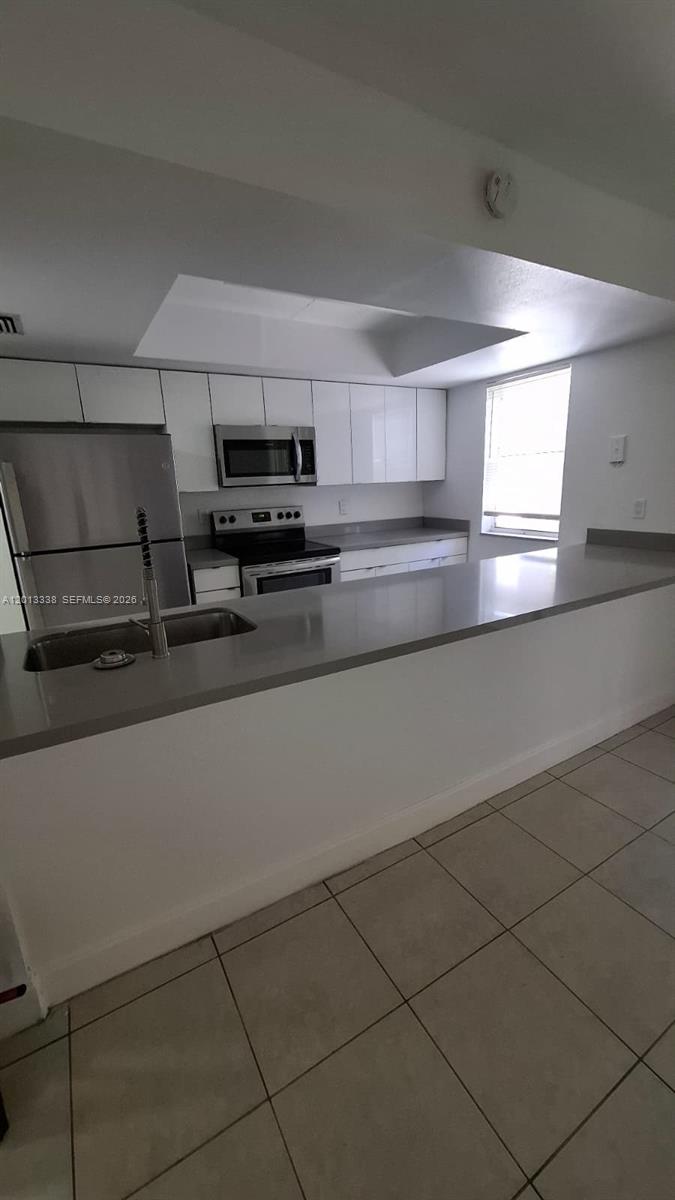 A kitchen features white cabinets, stainless steel appliances, and a gray countertop breakfast bar — 16220 NW 2nd Ave # 410, Miami FL 33169, MIAMI, FL