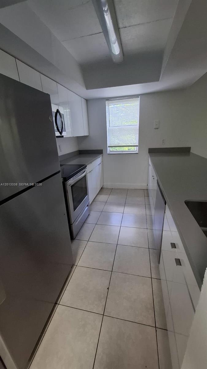 A galley-style kitchen features white cabinets, stainless steel appliances, and light-colored floor tiles — 16220 NW 2nd Ave # 410, Miami FL 33169, MIAMI, FL