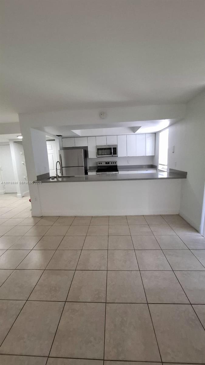 A kitchen with white cabinets, stainless steel appliances, and a breakfast bar overlooks a tiled room — 16220 NW 2nd Ave # 410, Miami FL 33169, MIAMI, FL