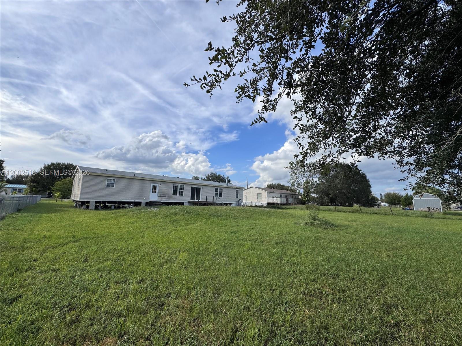 A wide shot of a manufactured home situated on a large, grassy lot — 866 NE 104, Okeechobee FL 34972, OKEECHOBEE, FL