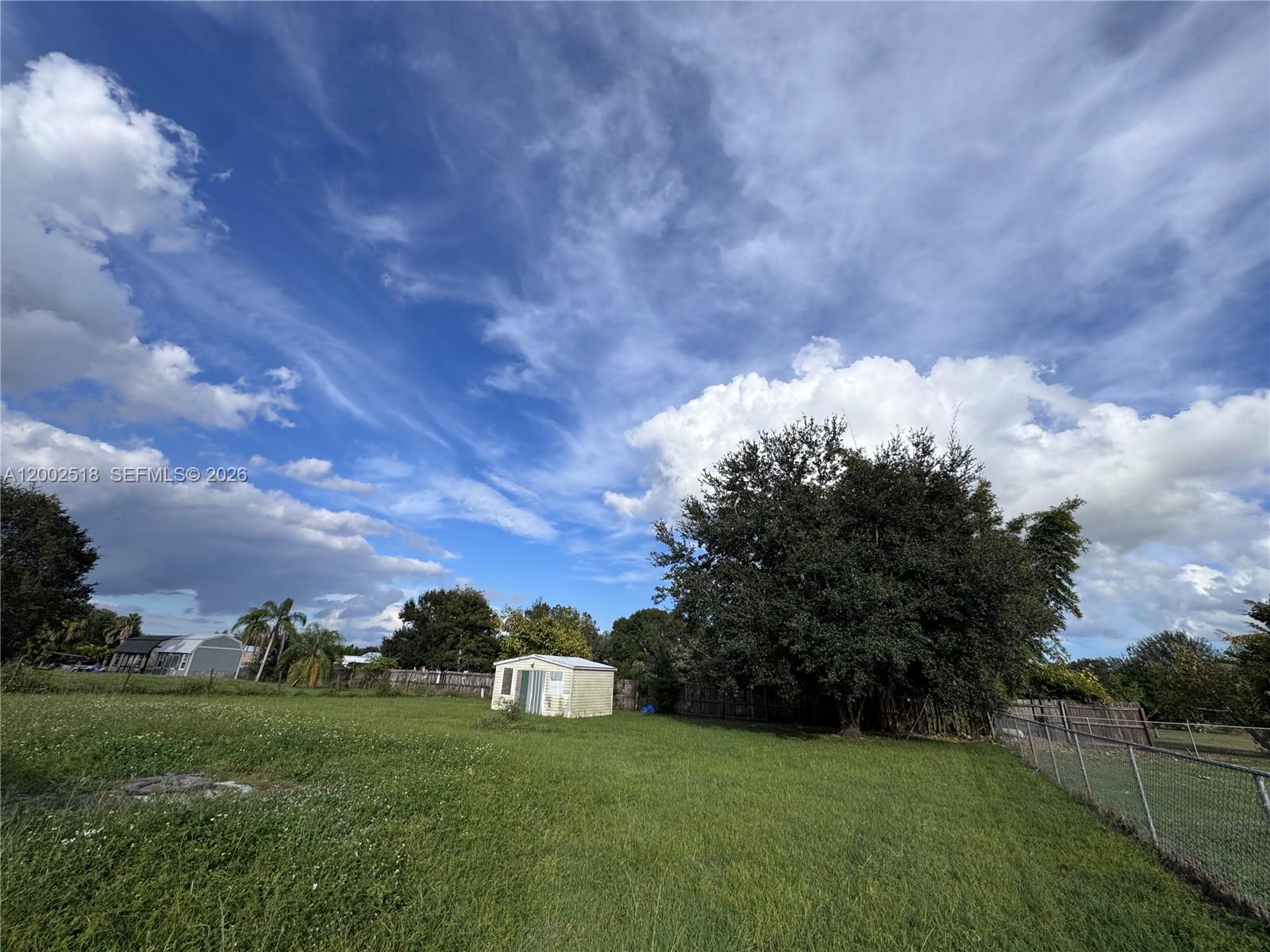 A grassy backyard features a small shed, a large tree, and a chain-link fence — 866 NE 104, Okeechobee FL 34972, OKEECHOBEE, FL