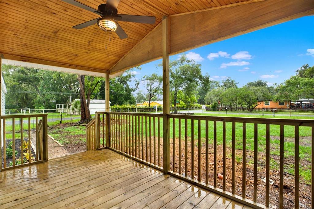 A covered wooden deck with a ceiling fan overlooks a grassy yard and surrounding trees — 5801 MYRTLE LANE, TAMPA, FL