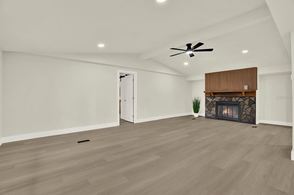 A living room features light wood-look flooring, a vaulted ceiling, and a stone fireplace — 5801 MYRTLE LANE, TAMPA, FL