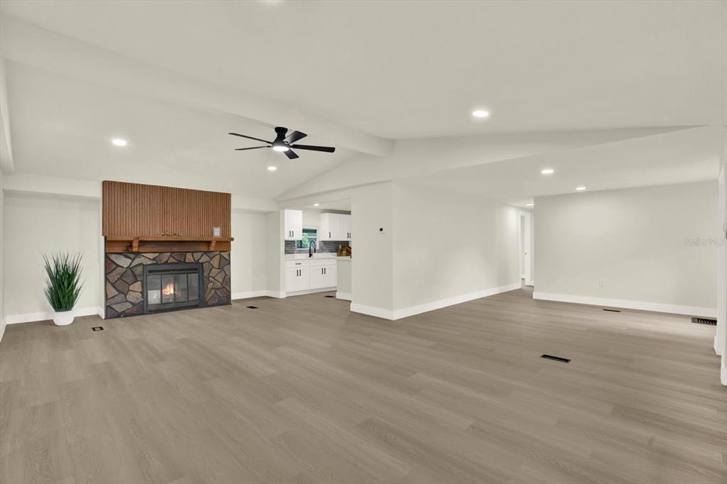 A spacious living room features light wood flooring, a stone fireplace, and a ceiling fan — 5801 MYRTLE LANE, TAMPA, FL