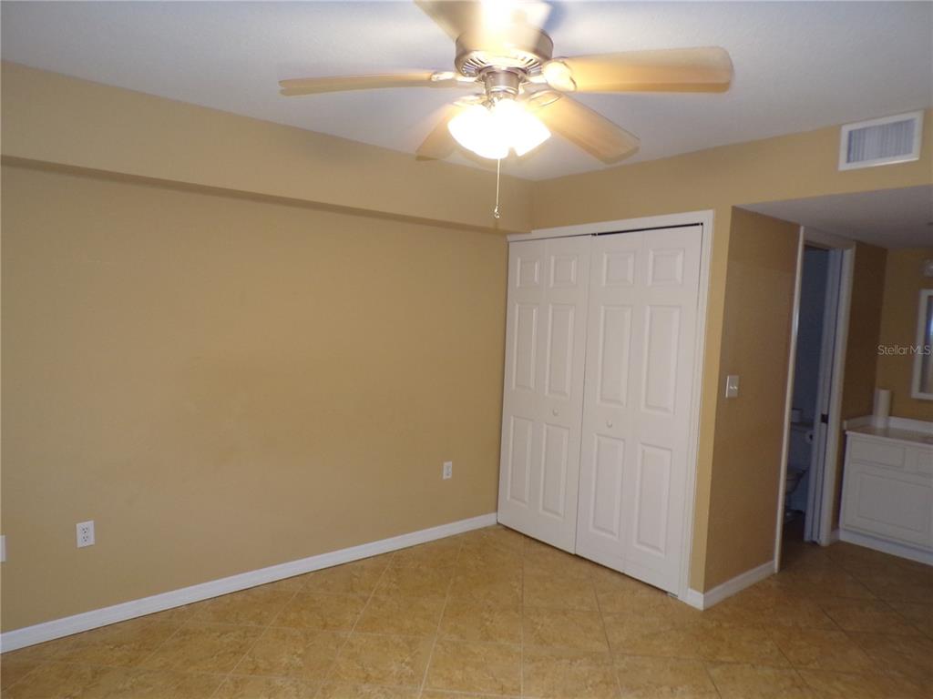 A bedroom with tan walls, tile flooring, a ceiling fan, and white closet doors — 150 HARBORSIDE AVENUE UNIT 133, PUNTA GORDA, FL