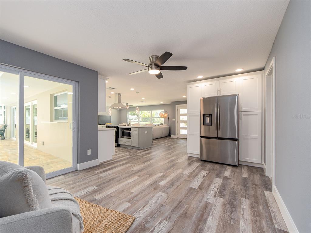 A kitchen and living area with wood-look flooring, white cabinetry, and a stainless steel refrigerator — 201 HARBOR BLUFF DRIVE, LARGO, FL
