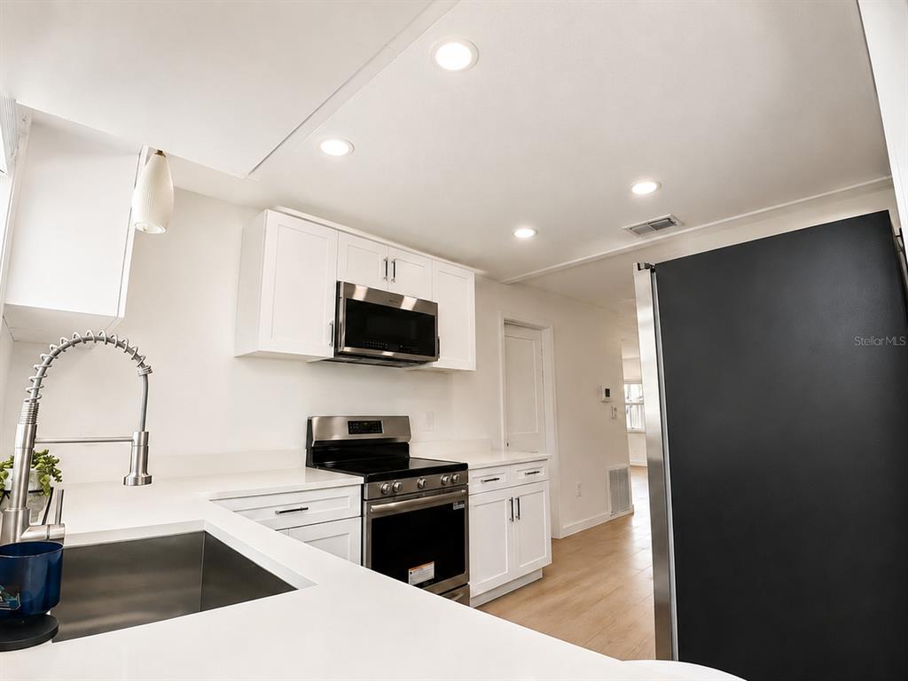 A modern kitchen features white cabinets, stainless steel appliances, and light wood-look flooring — 1834 NEW HAMPSHIRE AVENUE NE, ST PETERSBURG, FL