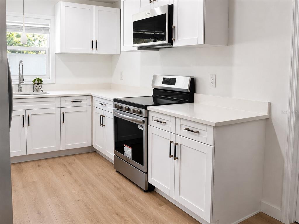 A modern kitchen features white cabinets, stainless steel appliances, and light wood-look flooring — 1834 NEW HAMPSHIRE AVENUE NE, ST PETERSBURG, FL
