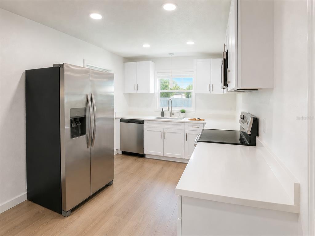 A kitchen features white cabinets, stainless steel appliances, and light wood-look flooring — 1834 NEW HAMPSHIRE AVENUE NE, ST PETERSBURG, FL