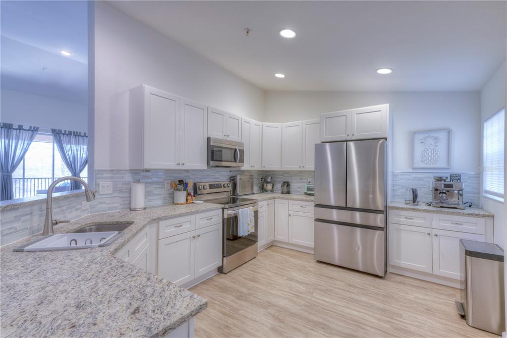 A kitchen features white cabinets, stainless steel appliances, granite countertops, and light wood-look flooring — 8318 FOSTER DRIVE UNIT 8318, DAVENPORT, FL