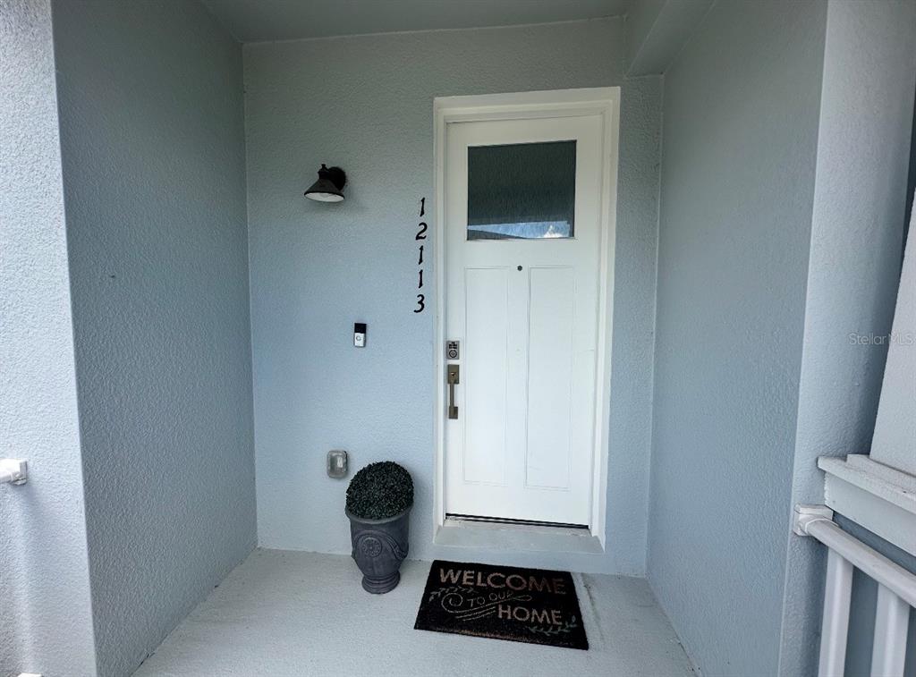 A white front door with a glass pane is set in a light blue entryway — 12113 VIA CASELLI LANE, WINDERMERE, FL