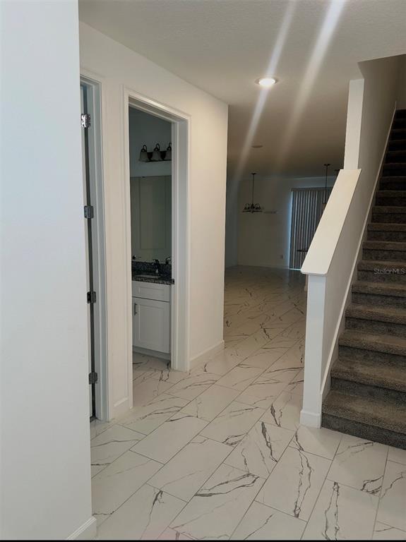 A hallway with white marble-look tile flooring leads to a bathroom and a staircase — 12113 VIA CASELLI LANE, WINDERMERE, FL