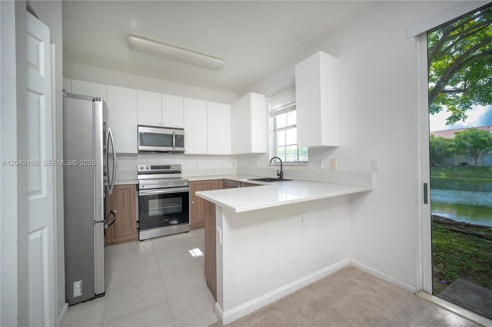 A kitchen features white upper cabinets, wood-tone lower cabinets, stainless steel appliances, and a lake view — 445 NE 21st Ave, Homestead FL 33033, HOMESTEAD, FL