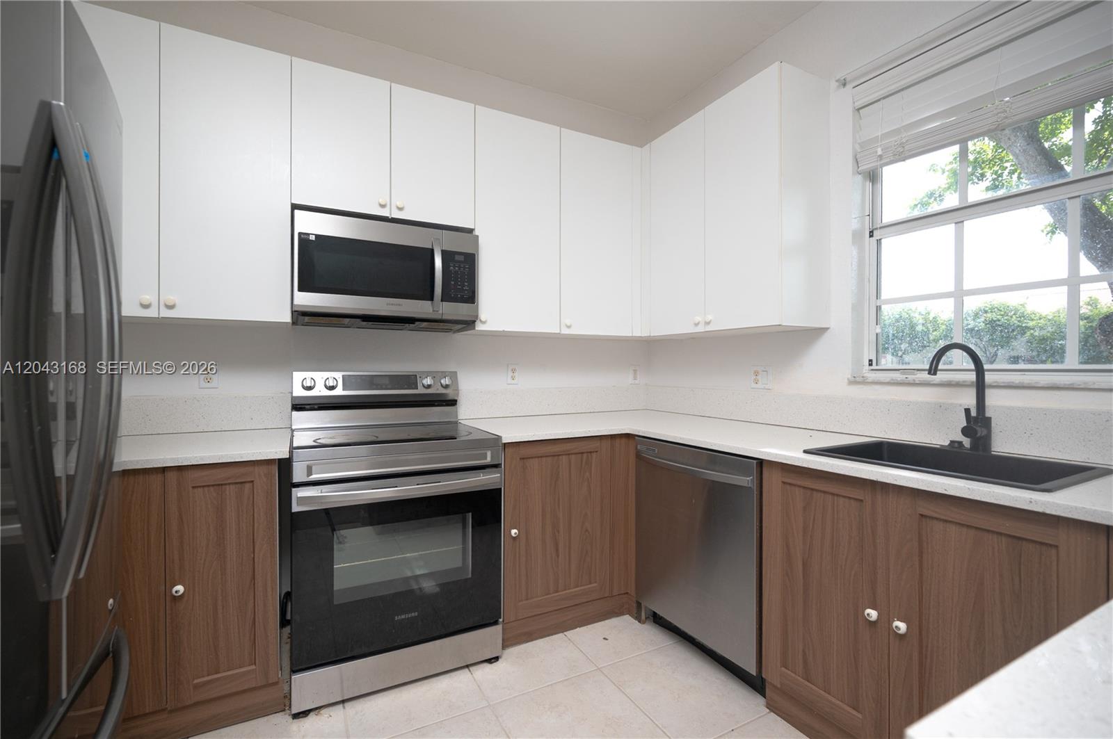 A kitchen features white upper cabinets, wood lower cabinets, stainless steel appliances, and a window — 445 NE 21st Ave, Homestead FL 33033, HOMESTEAD, FL