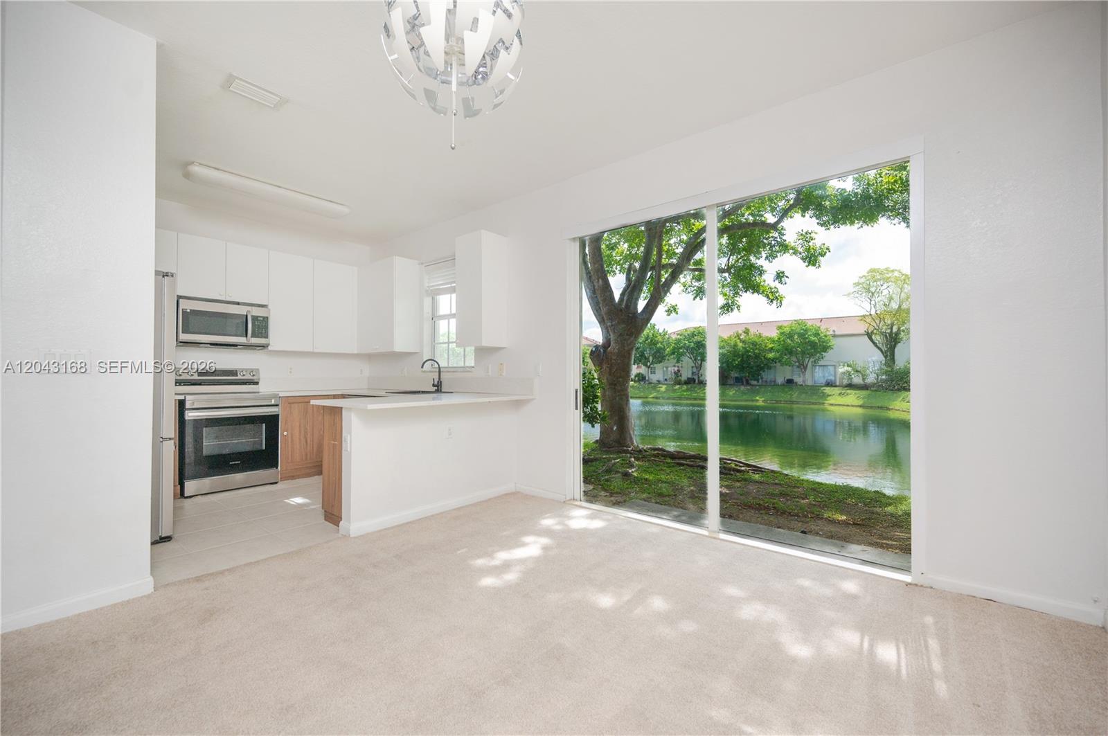 A kitchen with white cabinets and stainless steel appliances overlooks a lake through sliding doors — 445 NE 21st Ave, Homestead FL 33033, HOMESTEAD, FL