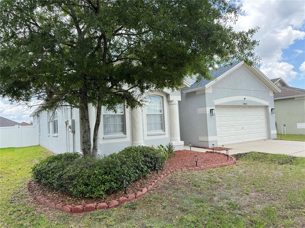 A light blue single-story house with a two-car garage and a landscaped front yard — 10868 STANDING STONE DRIVE, WIMAUMA, FL