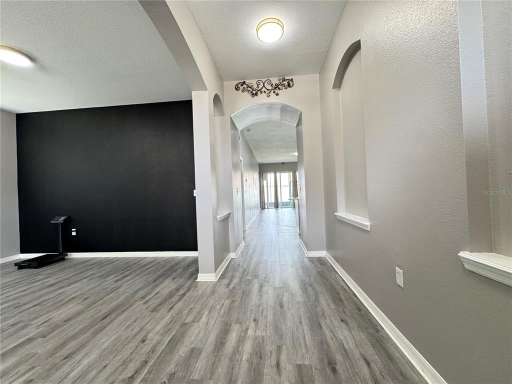 A hallway with gray wood-look flooring leads toward a bright room with glass doors — 10868 STANDING STONE DRIVE, WIMAUMA, FL