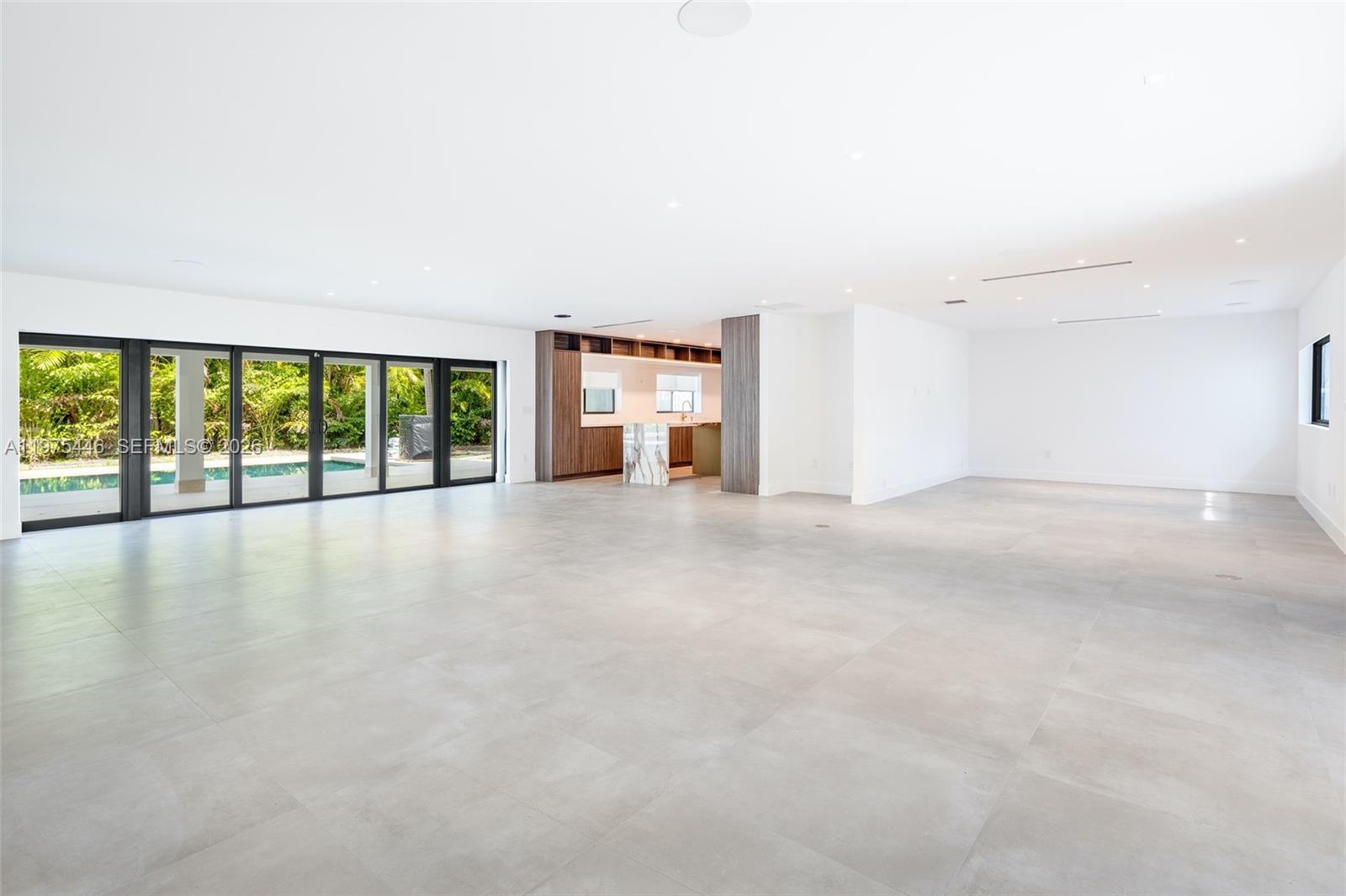 A spacious, minimalist living area features large glass sliding doors, light tile floors, and a kitchen — 13306 SW 58th Ct, Pinecrest FL 33156, PINECREST, FL