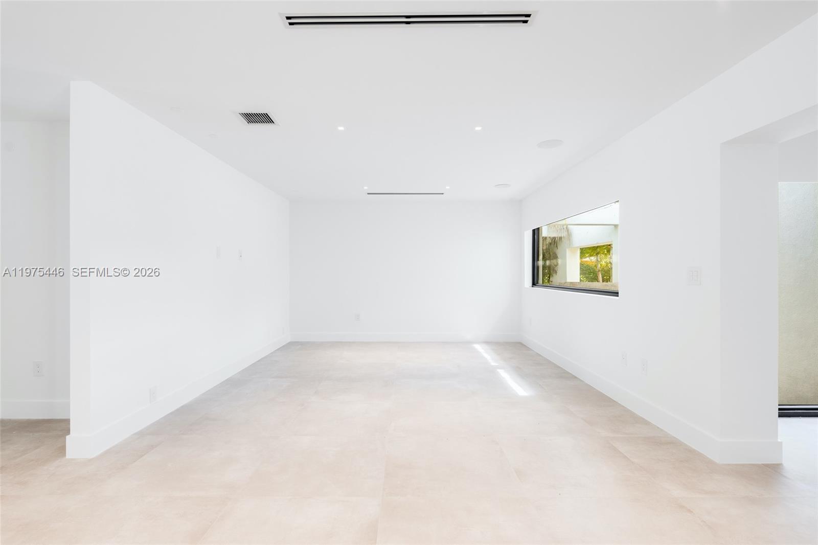 A minimalist, empty room features white walls, large light-colored floor tiles, and a horizontal window — 13306 SW 58th Ct, Pinecrest FL 33156, PINECREST, FL