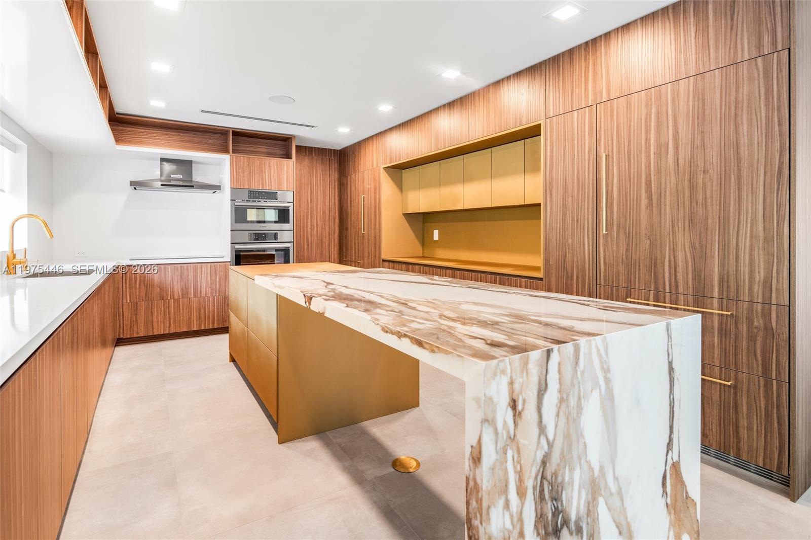 A modern kitchen features wood cabinetry, a marble waterfall island, and gold-toned accents — 13306 SW 58th Ct, Pinecrest FL 33156, PINECREST, FL