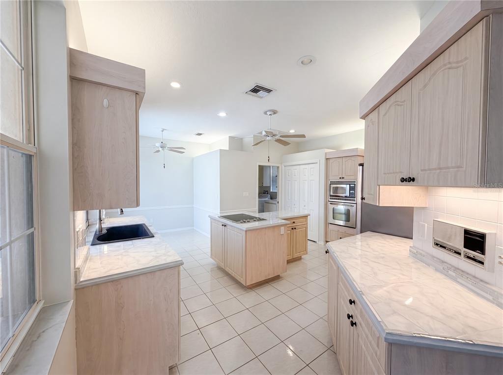 A kitchen features light wood cabinets, marble-patterned countertops, a center island, and white tile flooring — 3608 CREEKSIDE DRIVE, SEBRING, FL