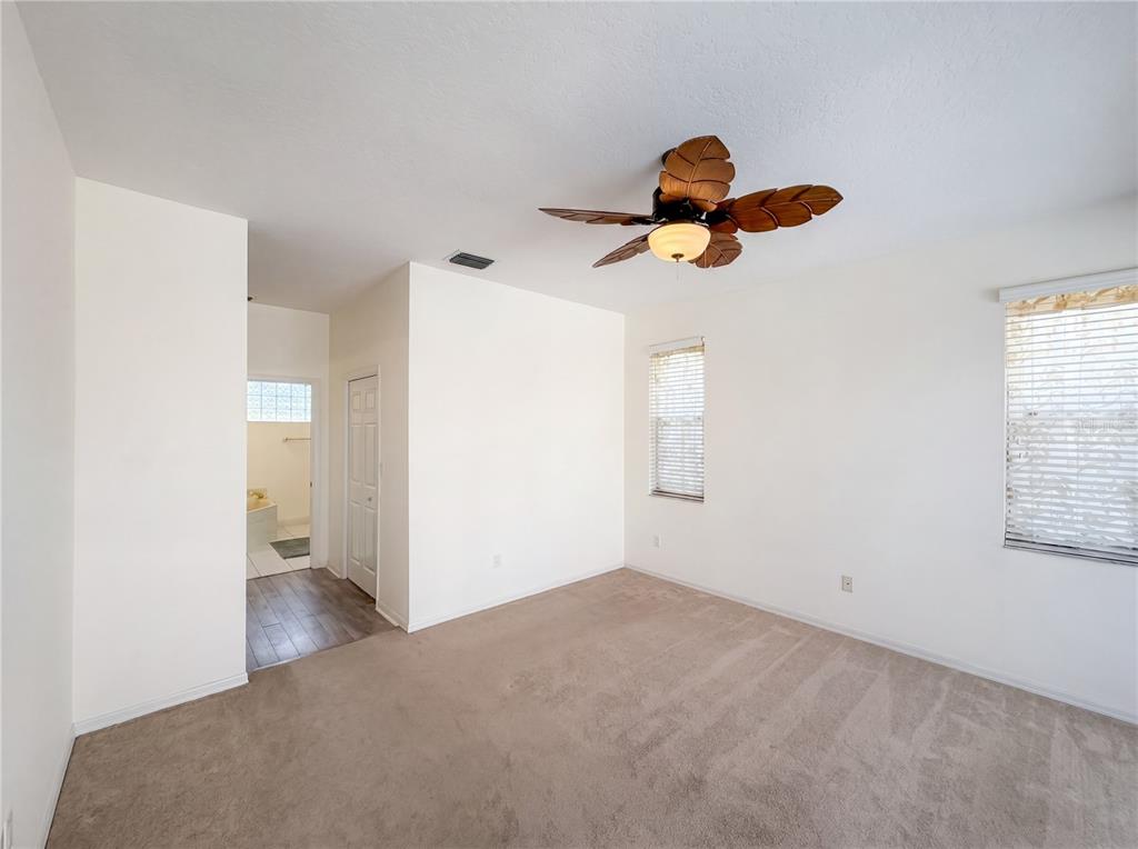 A bedroom with beige carpet, white walls, a palm-leaf ceiling fan, and an attached bathroom — 3608 CREEKSIDE DRIVE, SEBRING, FL