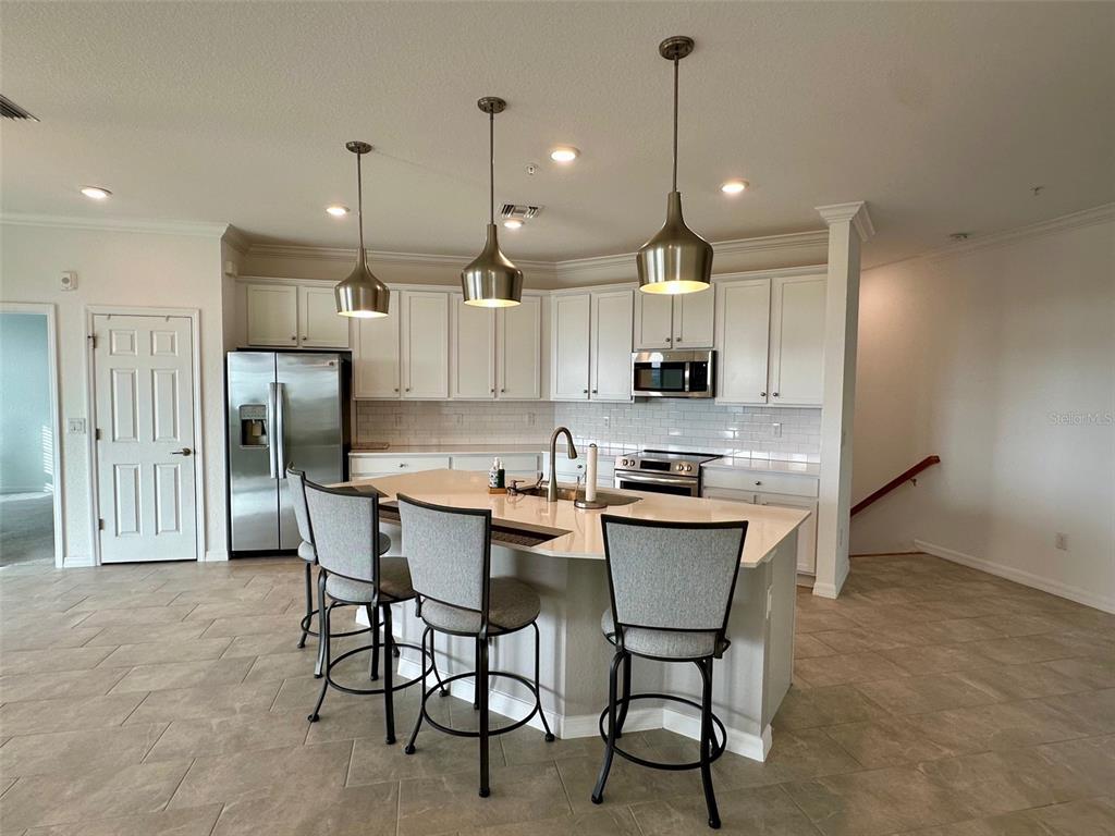 A kitchen features white cabinets, a central island with three bar stools, and pendant lighting — 10027 CROOKED CREEK DRIVE UNIT 201, VENICE, FL