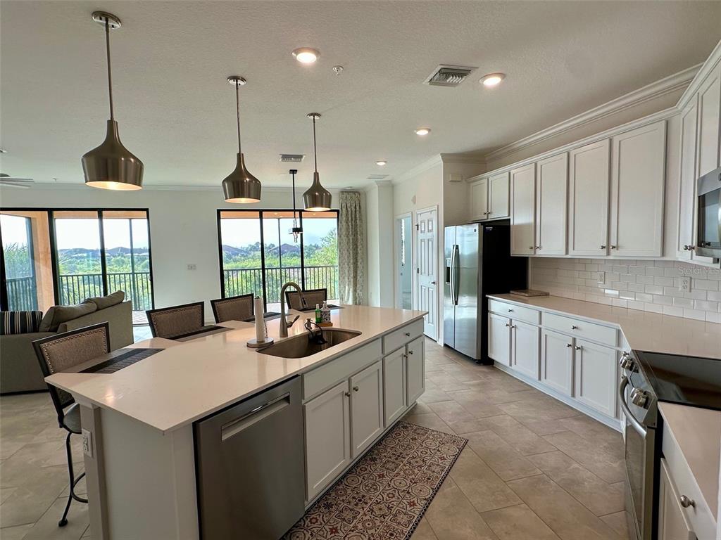 A kitchen features white cabinetry, a large island with a sink, and views of trees — 10027 CROOKED CREEK DRIVE UNIT 201, VENICE, FL