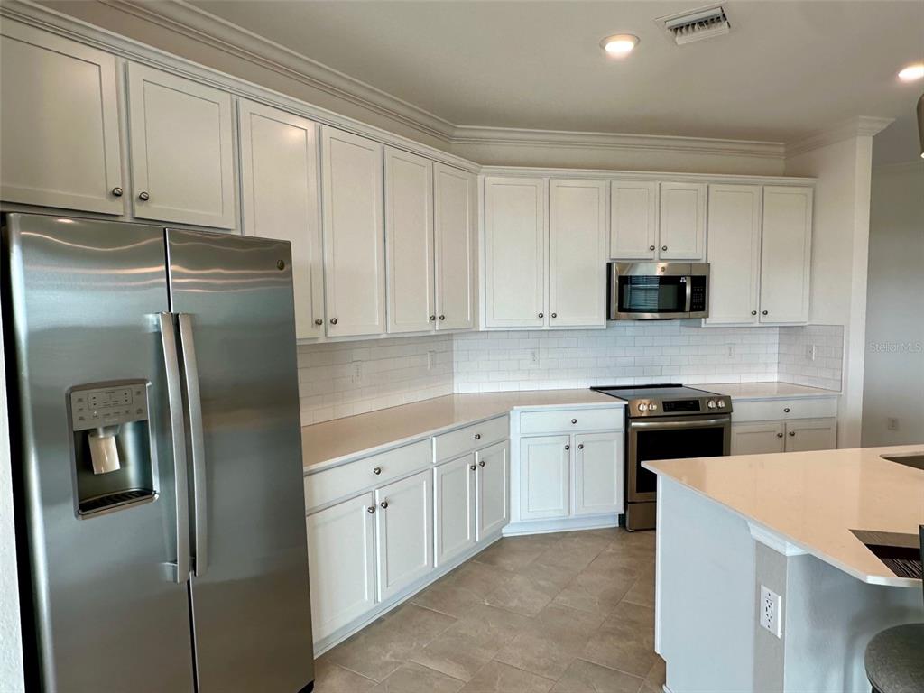 A kitchen features white cabinetry, stainless steel appliances, and light-colored countertops — 10027 CROOKED CREEK DRIVE UNIT 201, VENICE, FL