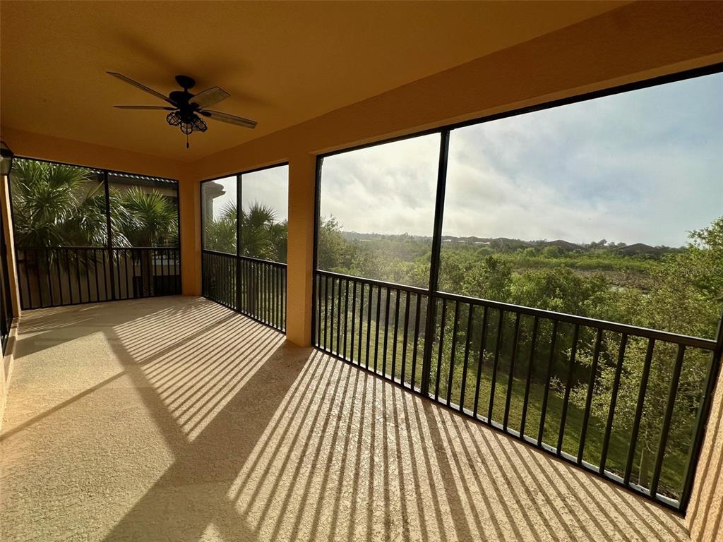 A screened-in balcony features a ceiling fan, beige flooring, and a view of trees — 10027 CROOKED CREEK DRIVE UNIT 201, VENICE, FL